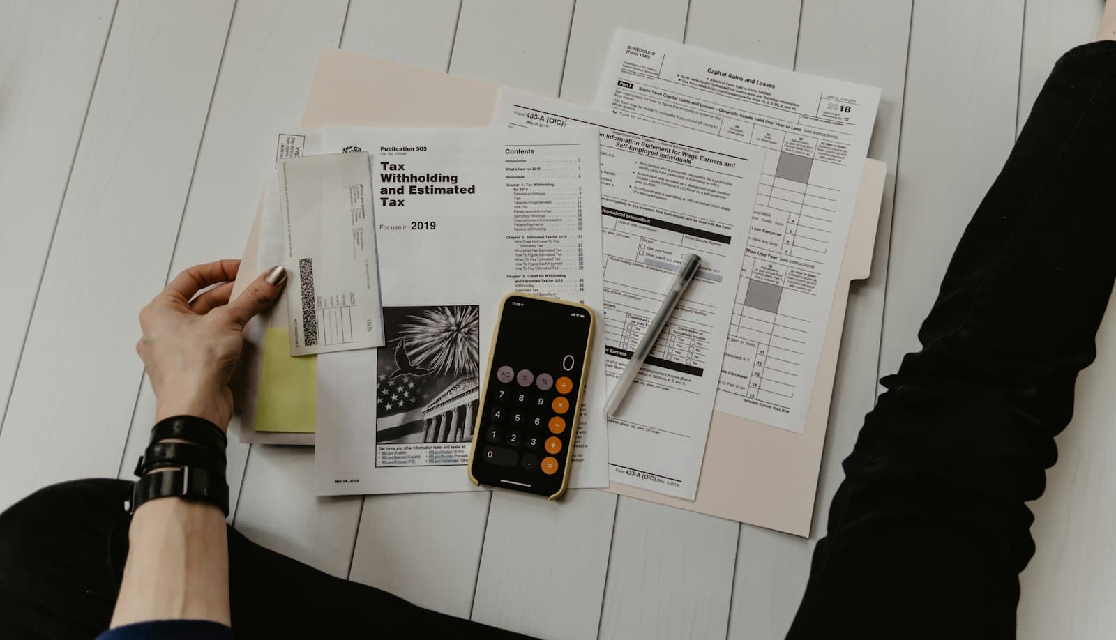 Hands reviewing tax forms beside a calculator and a phone on a desk
