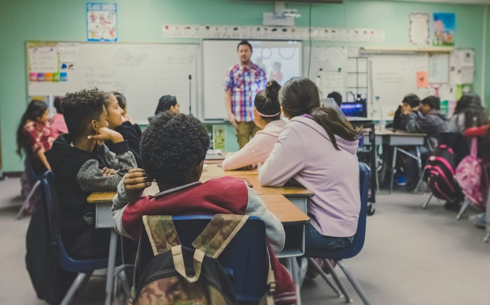Students at their desks listening to a teacher in a bright classroom