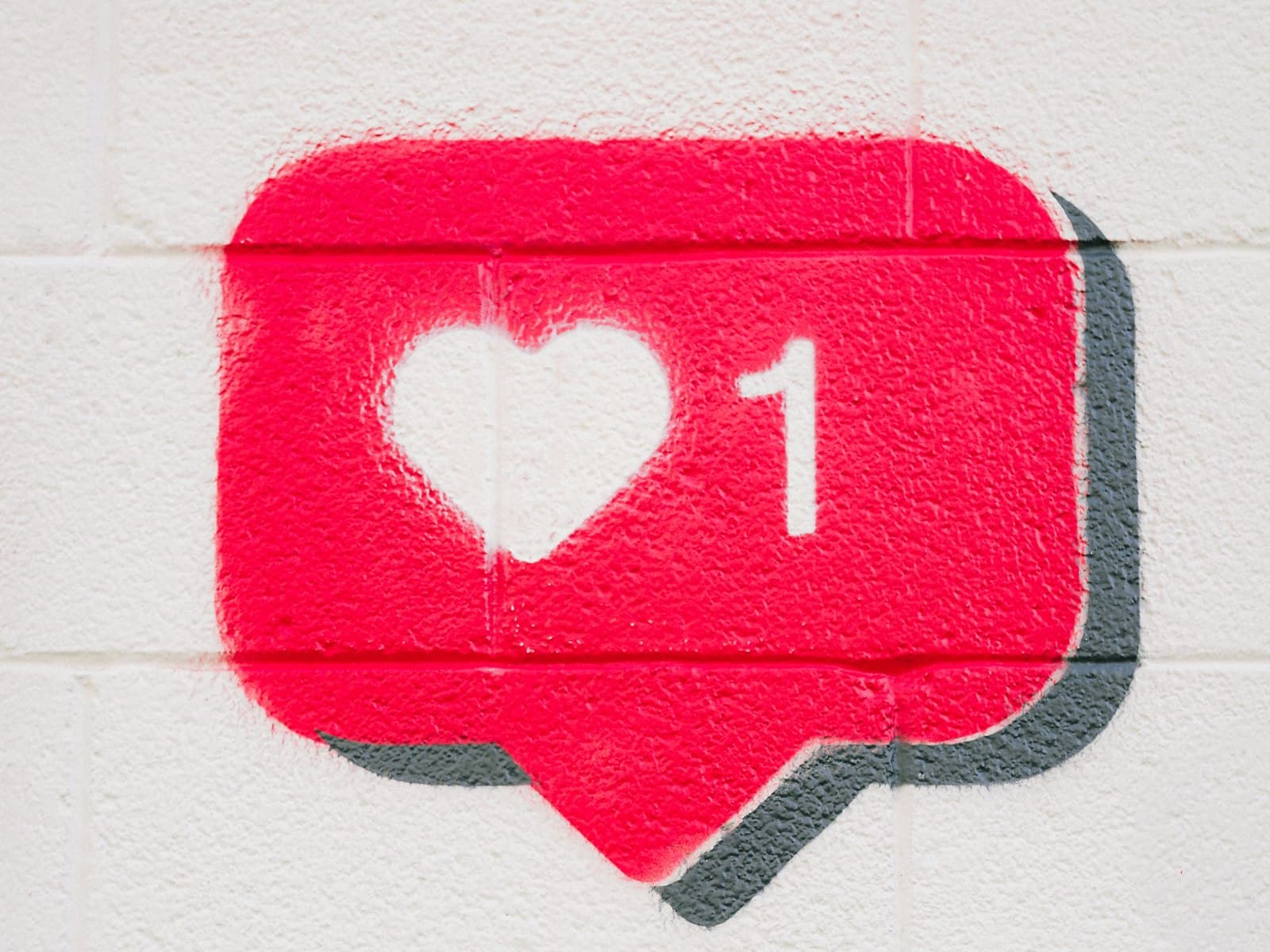 A red “like” notification painted on a white brick wall